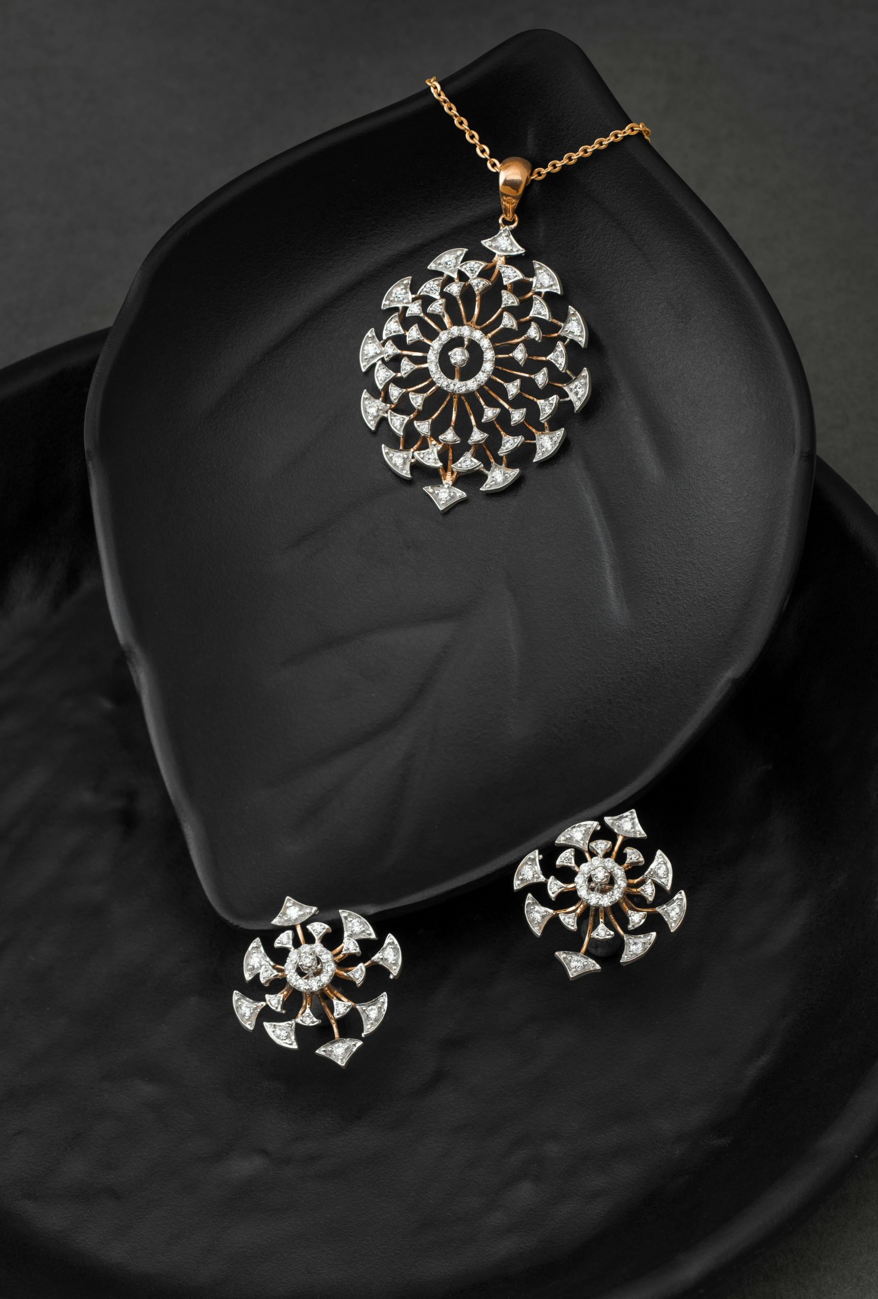 Luxurious gold and diamond jewelry set featuring a pendant and earrings on a black leaf-shaped surface.